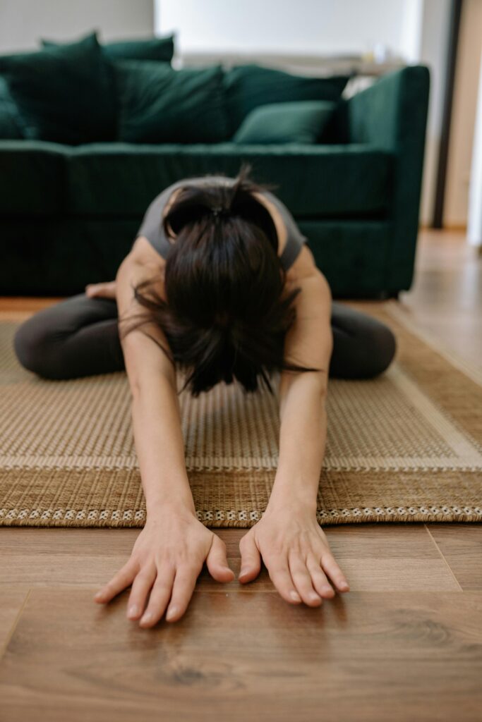 Woman performing yoga pose at home, stretching forward on a rug.